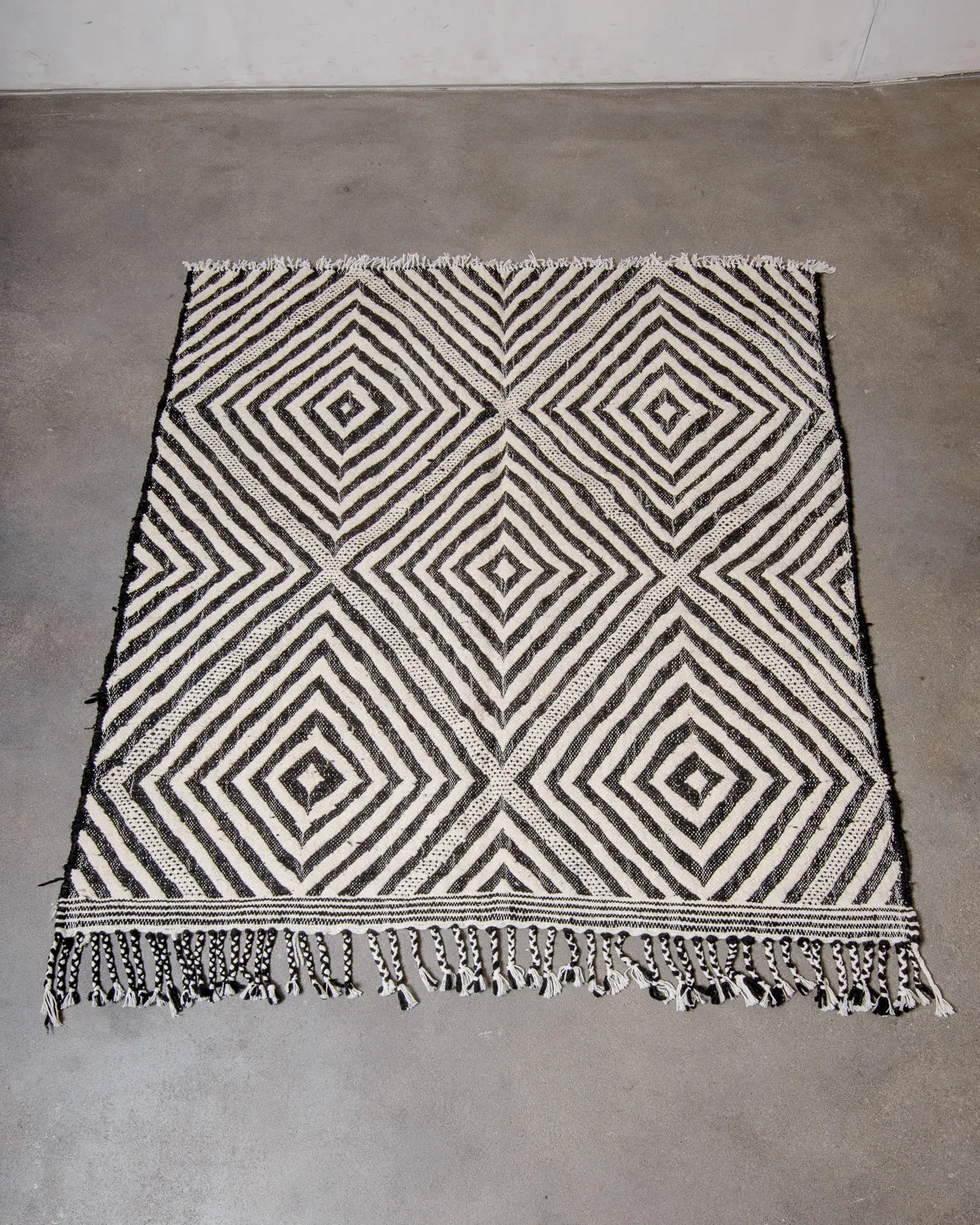 Berberlin Kelim Rug in black and white, laying on concrete studio floor.